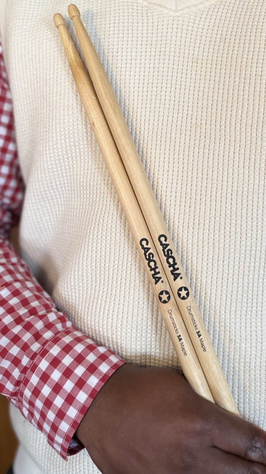 Primeiro plano de um par de baquetas Cascha 5A Maple seguras contra uma camisola clara